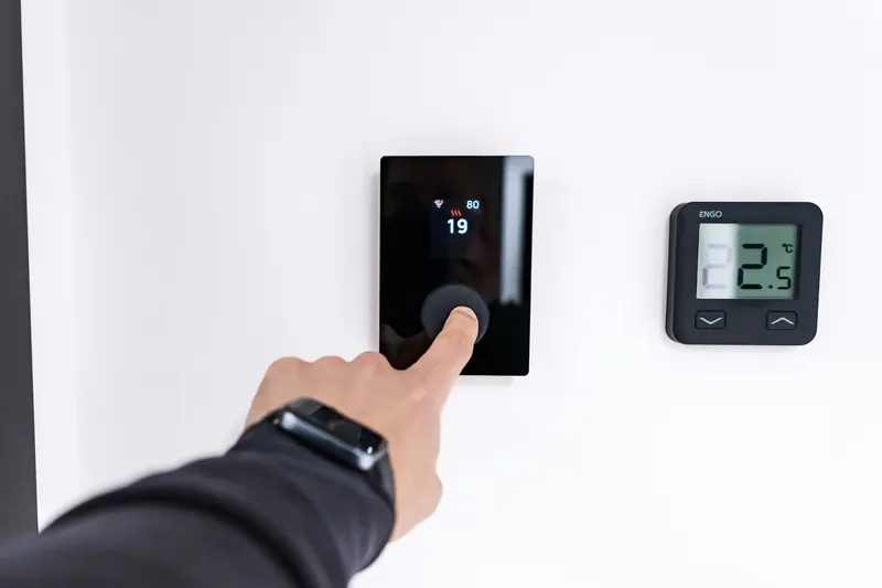 Hand adjusting a wall-mounted room controller next to a temperature sensor